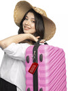 Smiling woman with a hat carrying a pink suitcase with a red 'Medical Supply Bag Handle With Care' luggage tag attached.