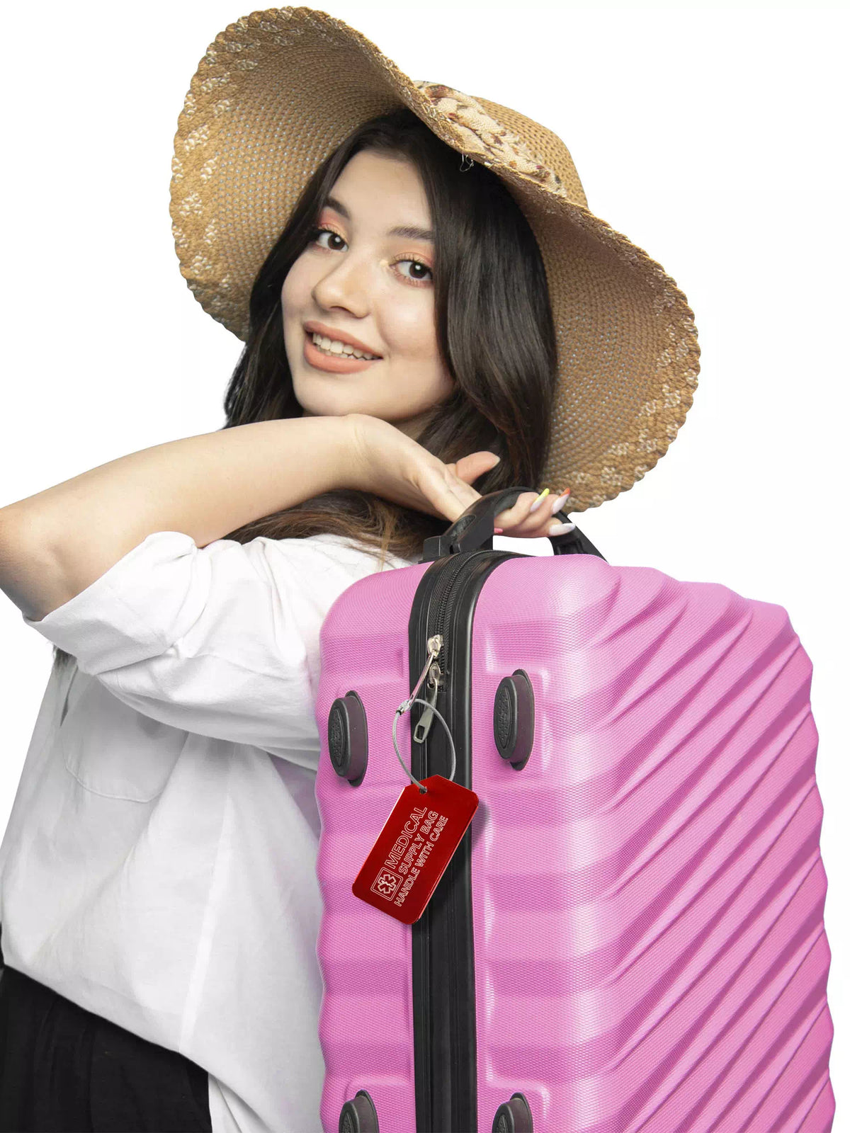 Smiling woman with a hat carrying a pink suitcase with a red 'Medical Supply Bag Handle With Care' luggage tag attached.